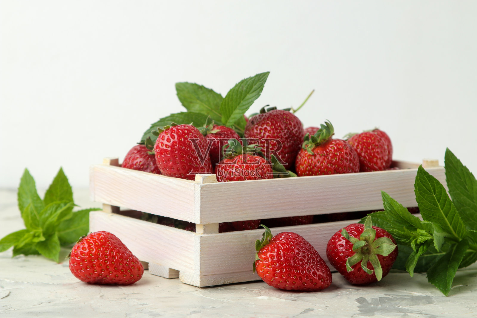 成熟、美味的草莓。木盒子里装着红草莓,轻水泥桌上放着薄荷叶。照片摄影图片