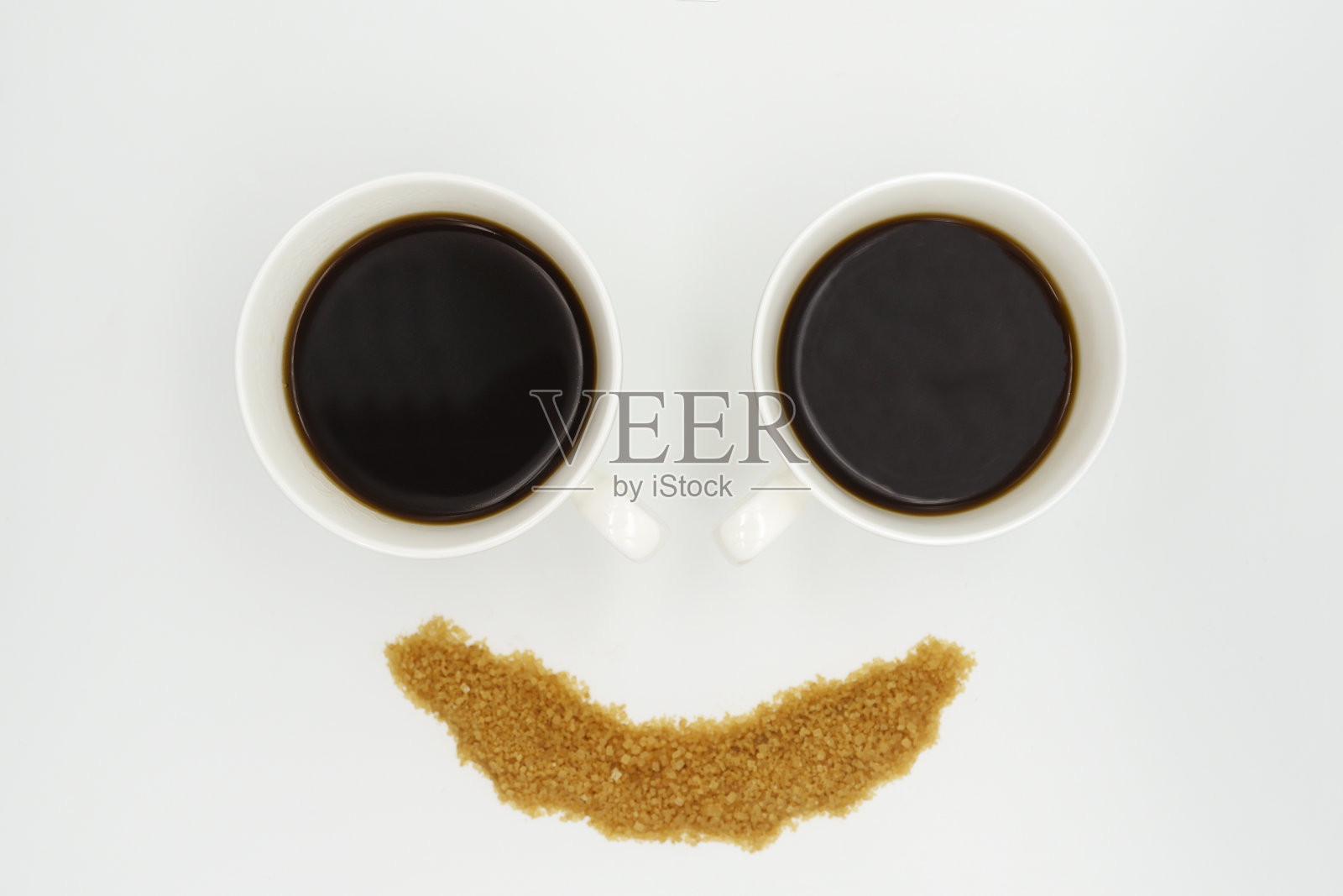 两个瓷咖啡杯,里面盛着美式咖啡,撒上白底笑脸形状的糖照片摄影图片