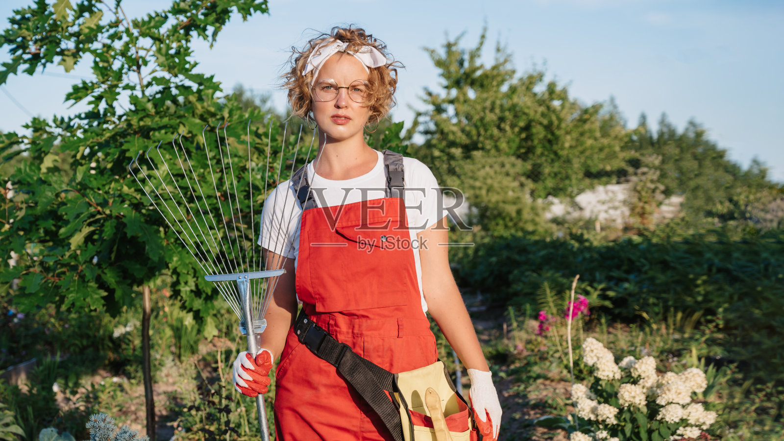 一位戴着手套、系着围裙的快乐女园丁站在家庭花园花坛的背景下。园艺和花卉栽培。花护理照片摄影图片