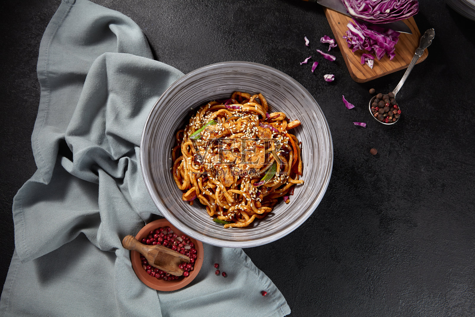 头顶上,鸡肉和蔬菜炒乌冬面,在黑色背景上漂亮地摆放着,还有香料和餐巾照片摄影图片