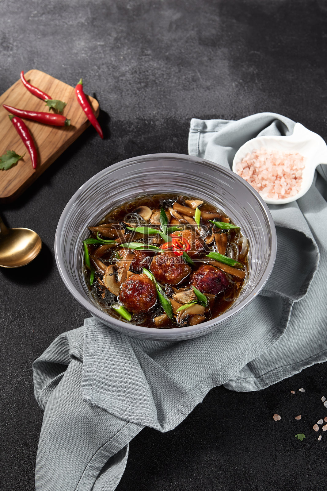 亚洲风味汤:蘑菇肉丸,黑色背景上艺术呈现,搭配新鲜食材和精致餐巾照片摄影图片