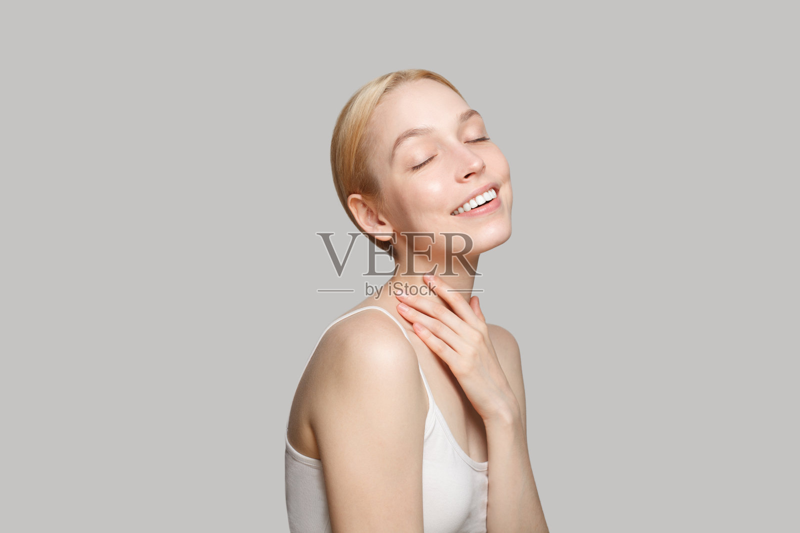 快乐的金发女人侧身站在灰色的背景上。美容、化妆品、护肤照片摄影图片