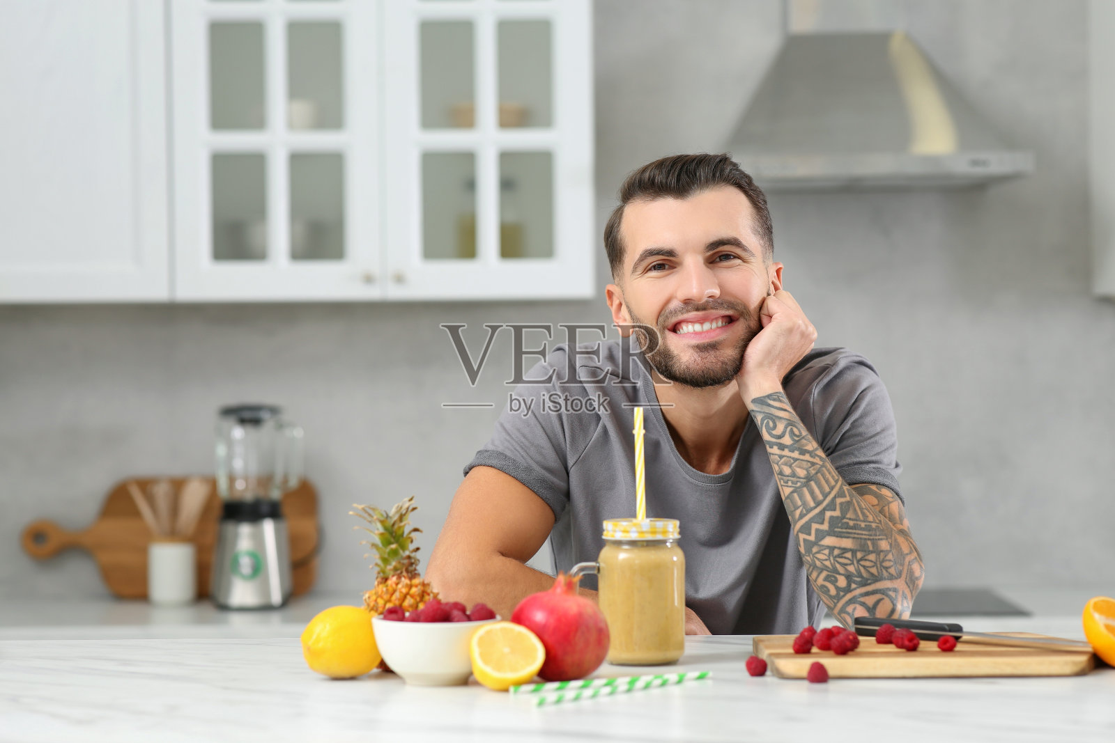 帅气的男人在厨房的白色桌子上享用美味的冰沙和食材。文本空间照片摄影图片