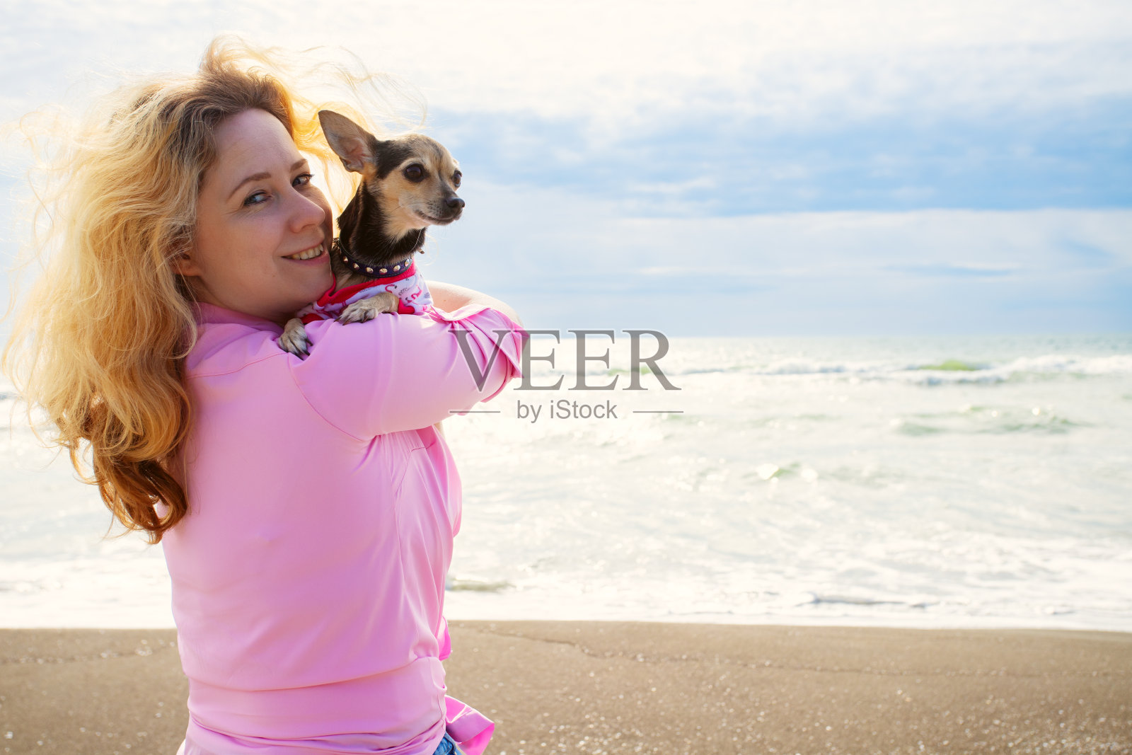 一个快乐的女人在阳光明媚的日子里和她顽皮的狗在沙滩上散步,带着宠物旅行,暑假照片摄影图片