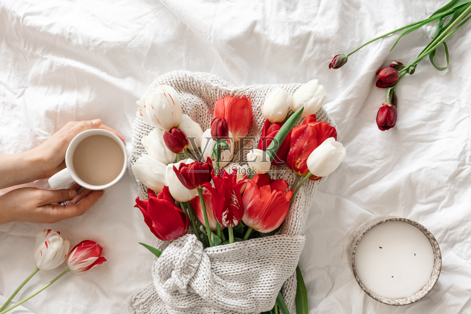 白色的床上,一个女人手里拿着一束花和一杯咖啡。照片摄影图片