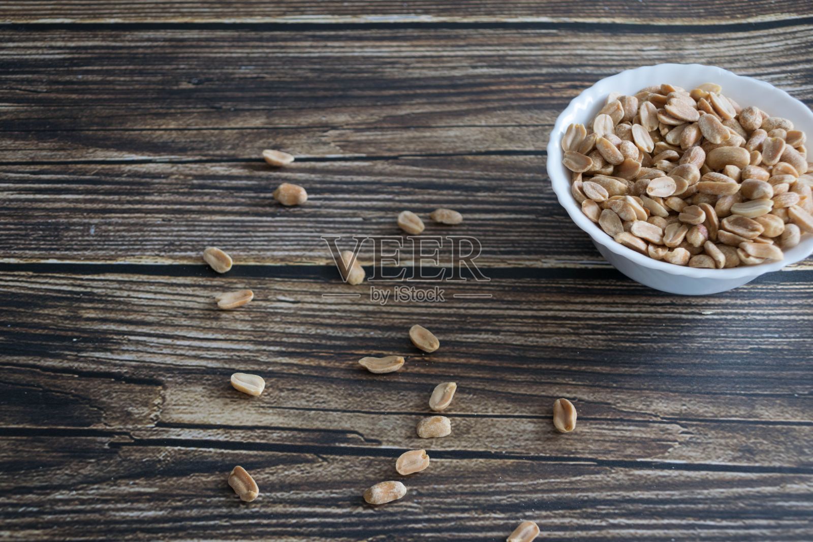 白色的陶瓷碗里盛满了花生,放在木桌上照片摄影图片