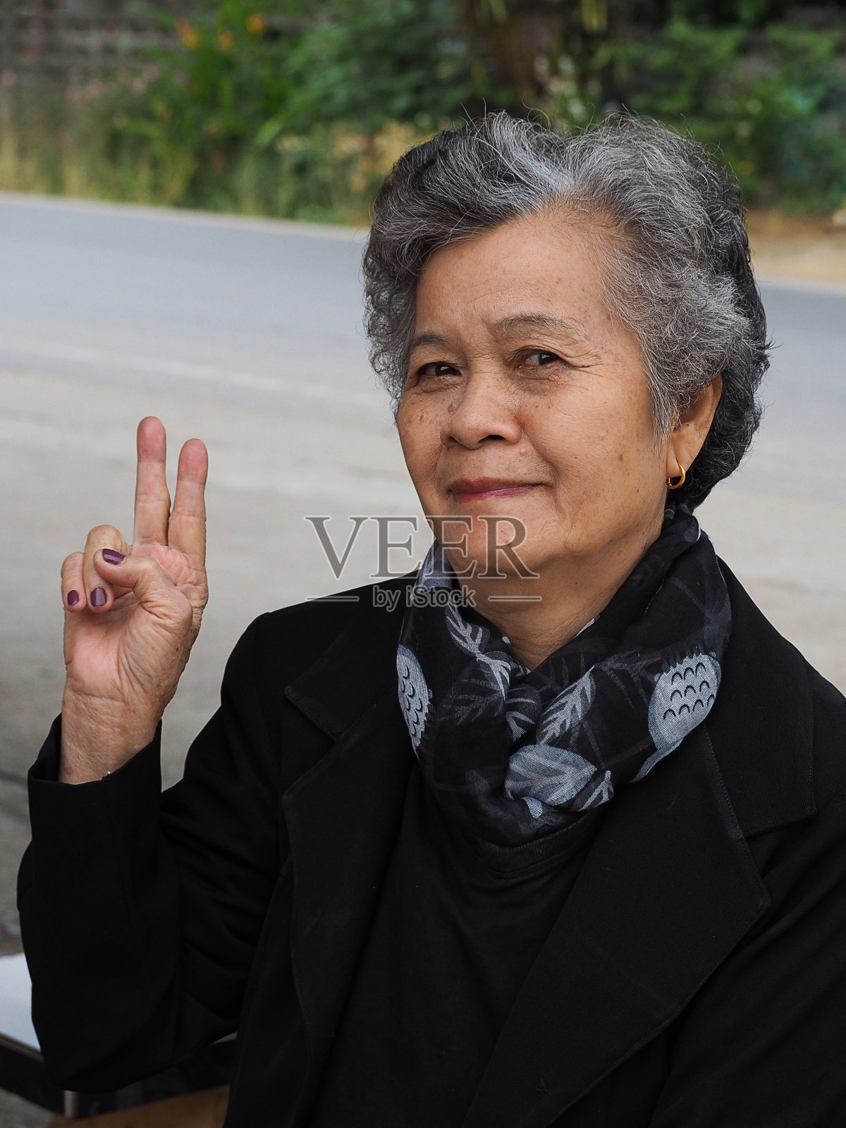 一位年长的女性坐在户外,看着镜头,微笑着做出胜利的手势。照片摄影图片