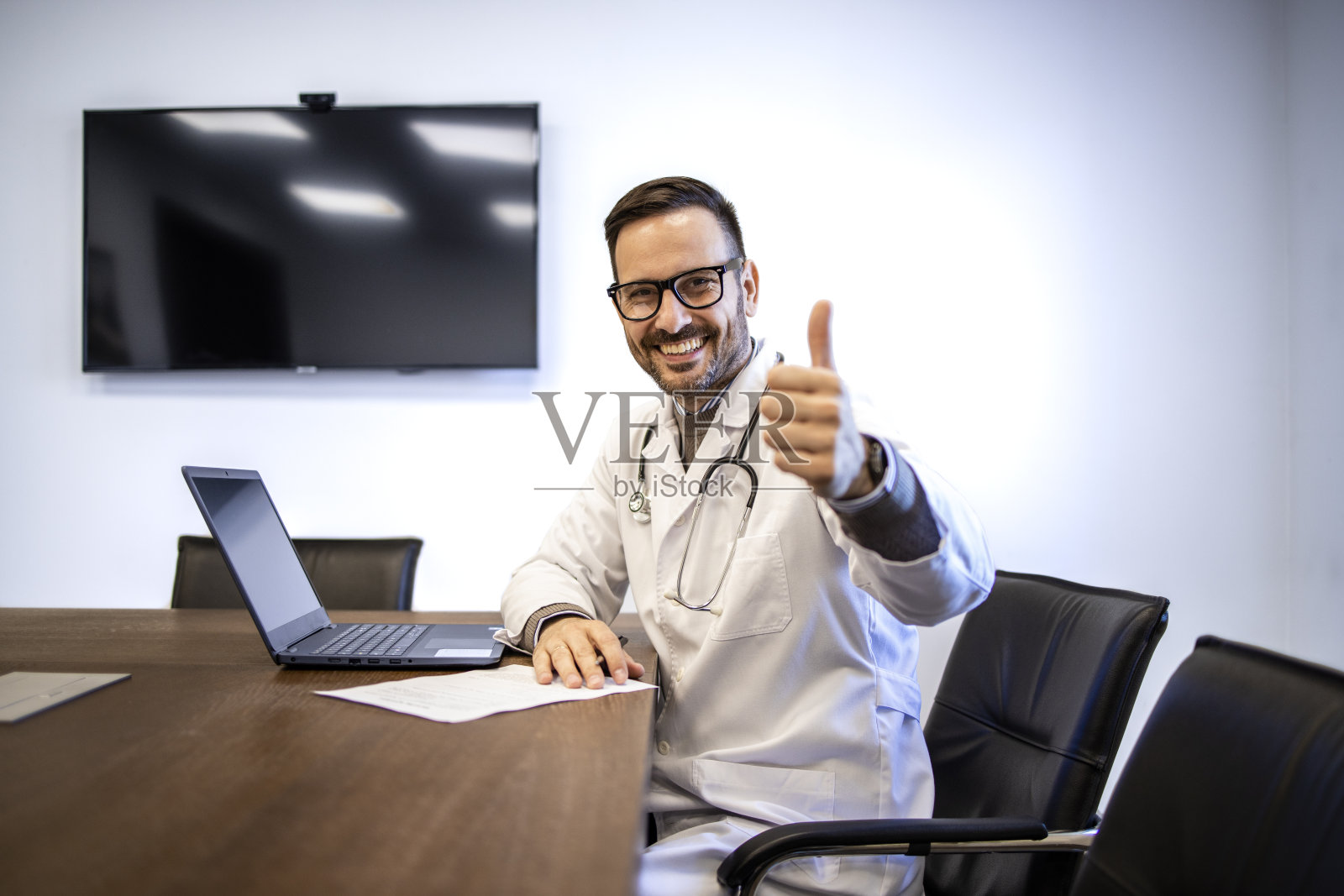 白人医生坐在办公室里竖起大拇指。照片摄影图片