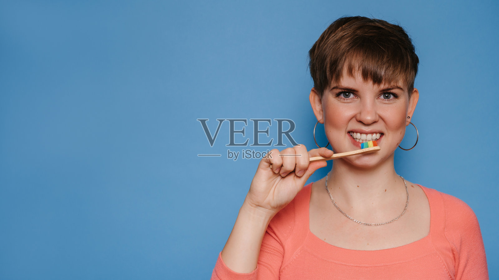 一个微笑的年轻女子拿着一把天然的竹牙刷,孤立在蓝色的背景上。口腔卫生的概念。放文字的地方。照片摄影图片