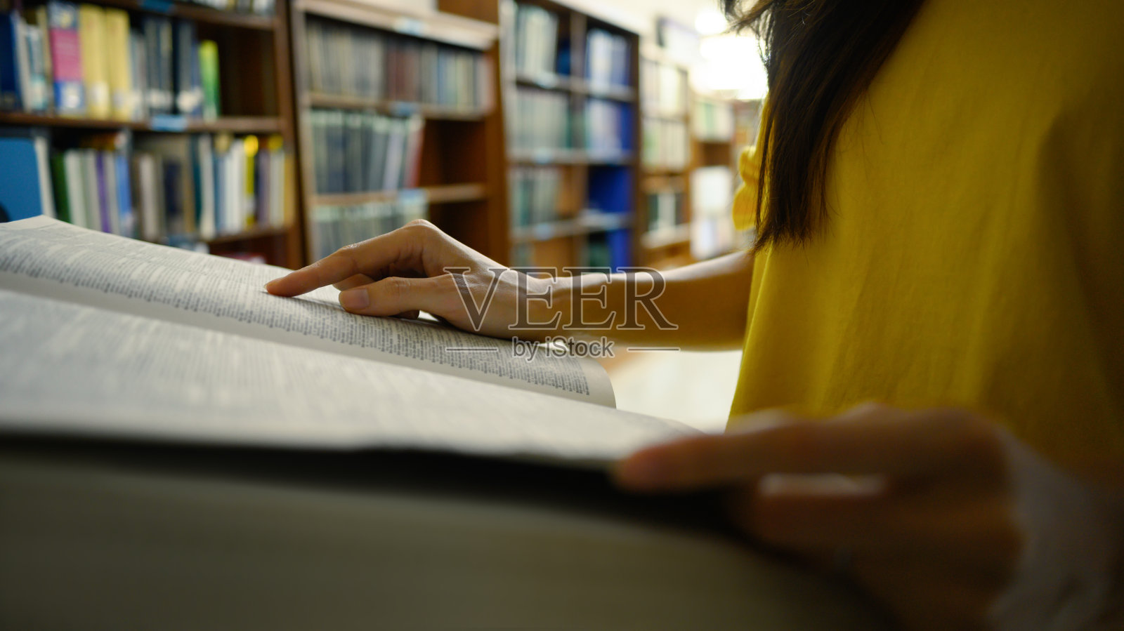 年轻女子坐在书架旁边的地板上,阅读课本,做研究,准备考试。照片摄影图片