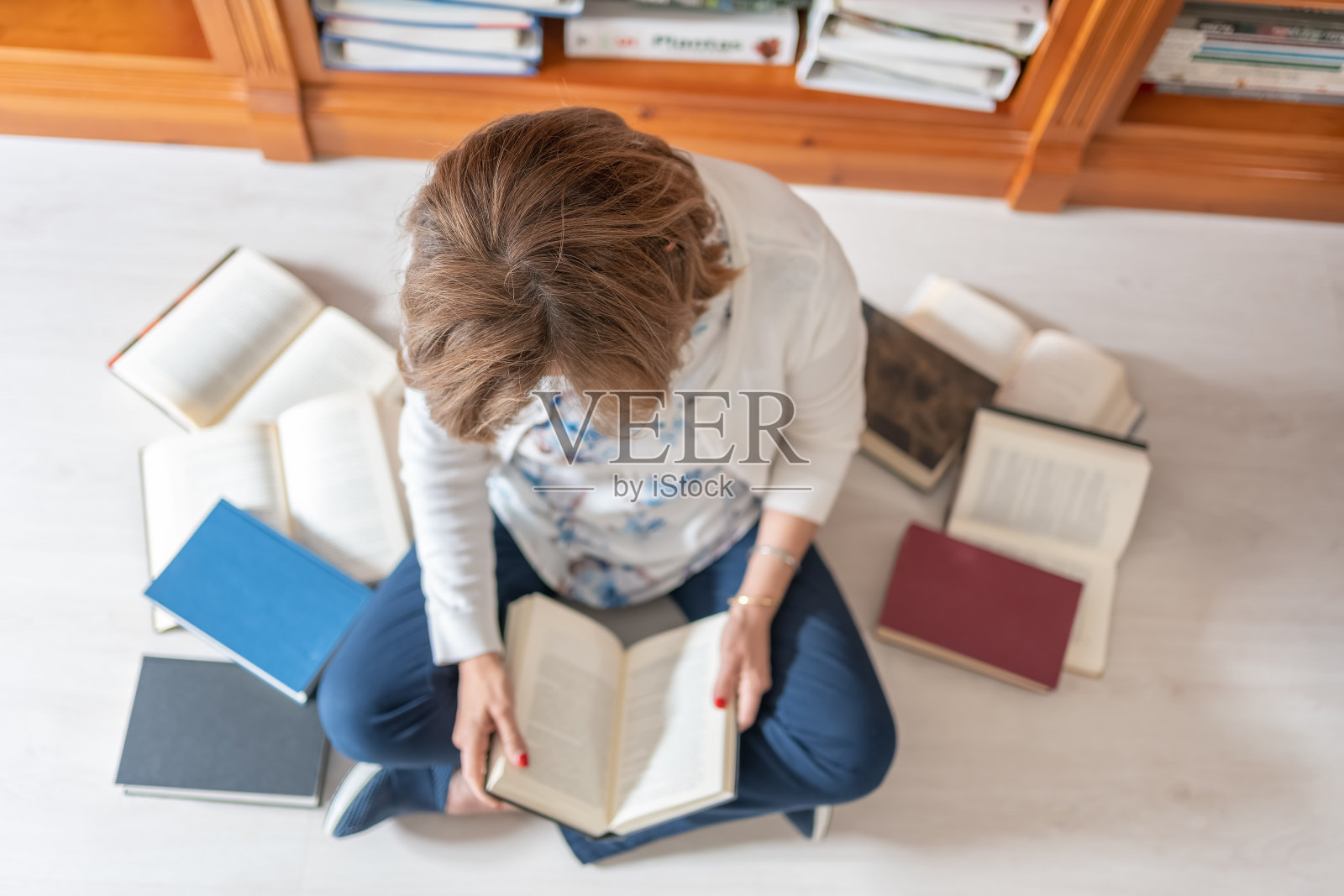 一个白人妇女坐在地板上,头顶上有一张照片,上面有很多书照片摄影图片