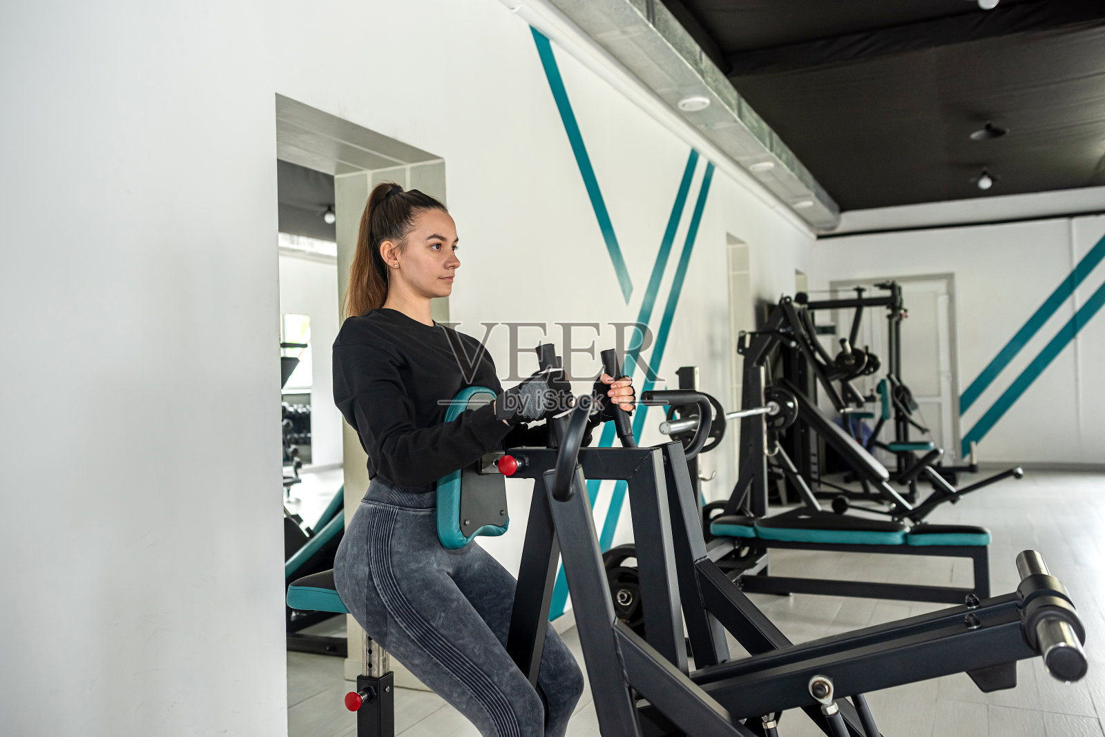 迷人的黑发女孩在模拟器上锻炼身体。照片摄影图片