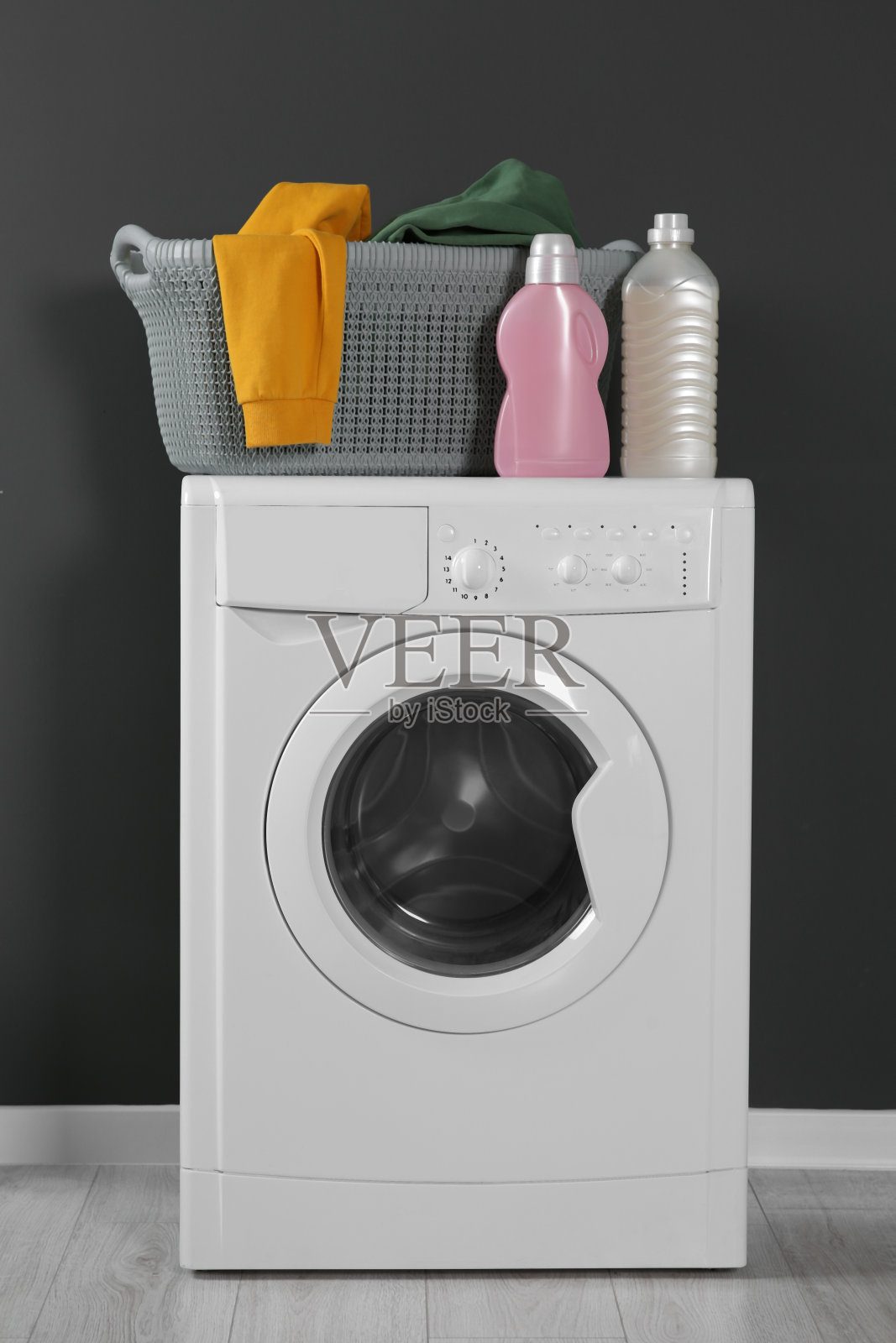 洗衣机与衣物和洗涤剂靠近室内黑墙。室内设计照片摄影图片