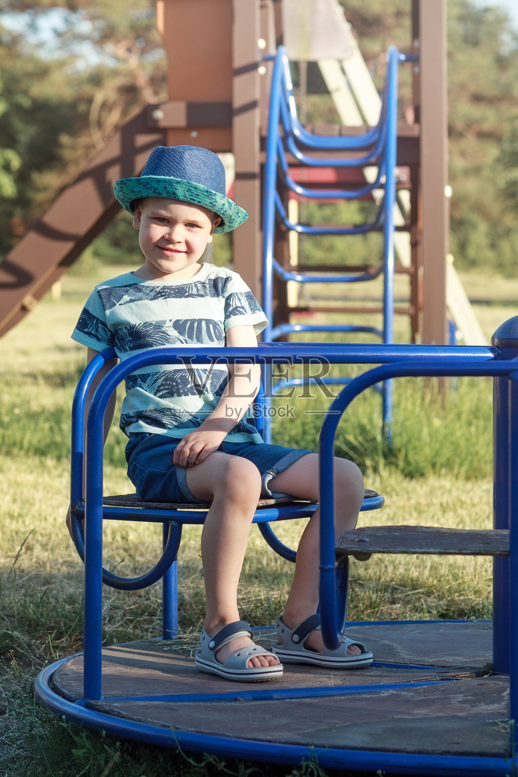 一个开朗、轻松的小男孩坐在操场上的旋转木马上休息照片摄影图片