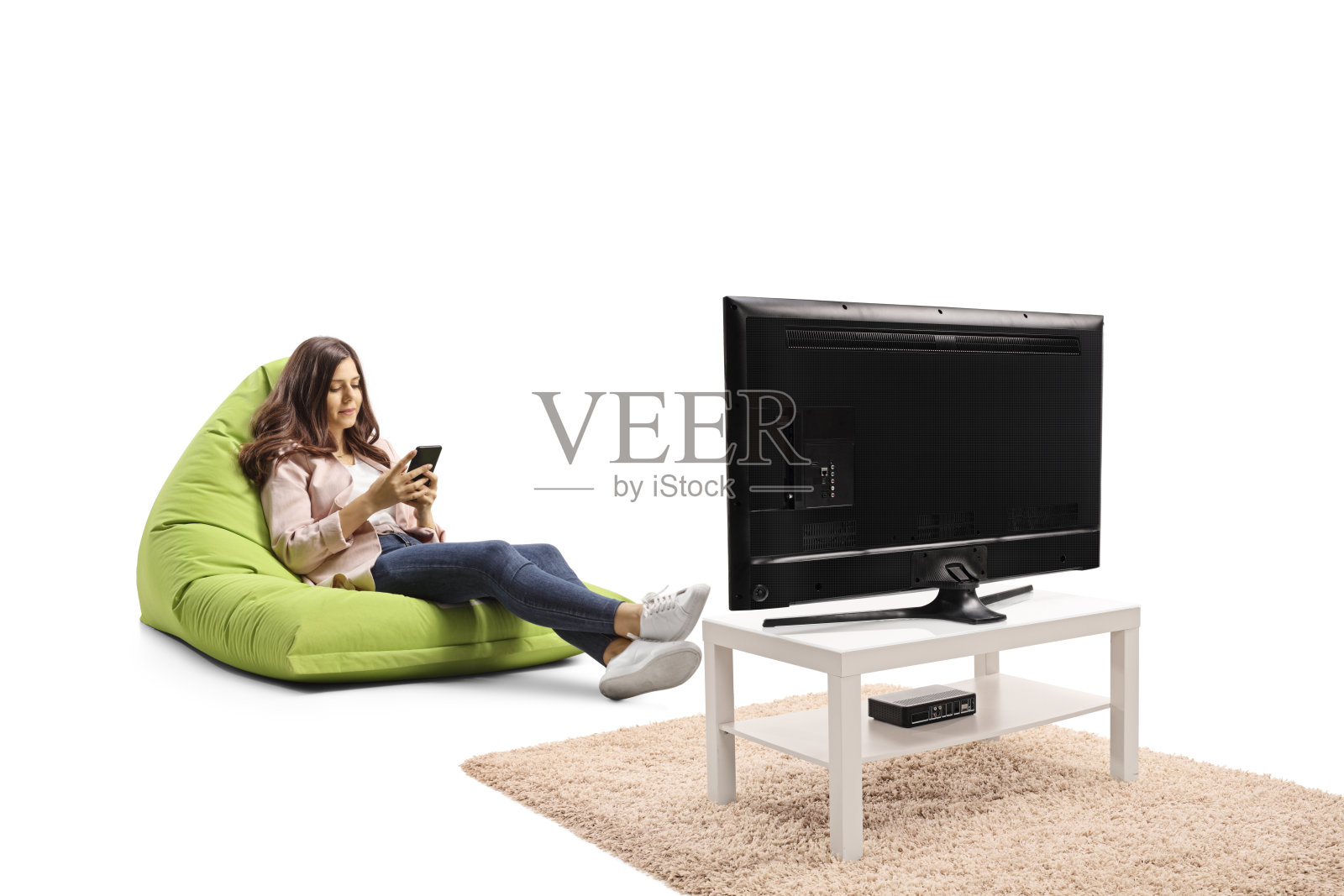 一个年轻女人坐在沙发上看电视,手里拿着智能手机照片摄影图片