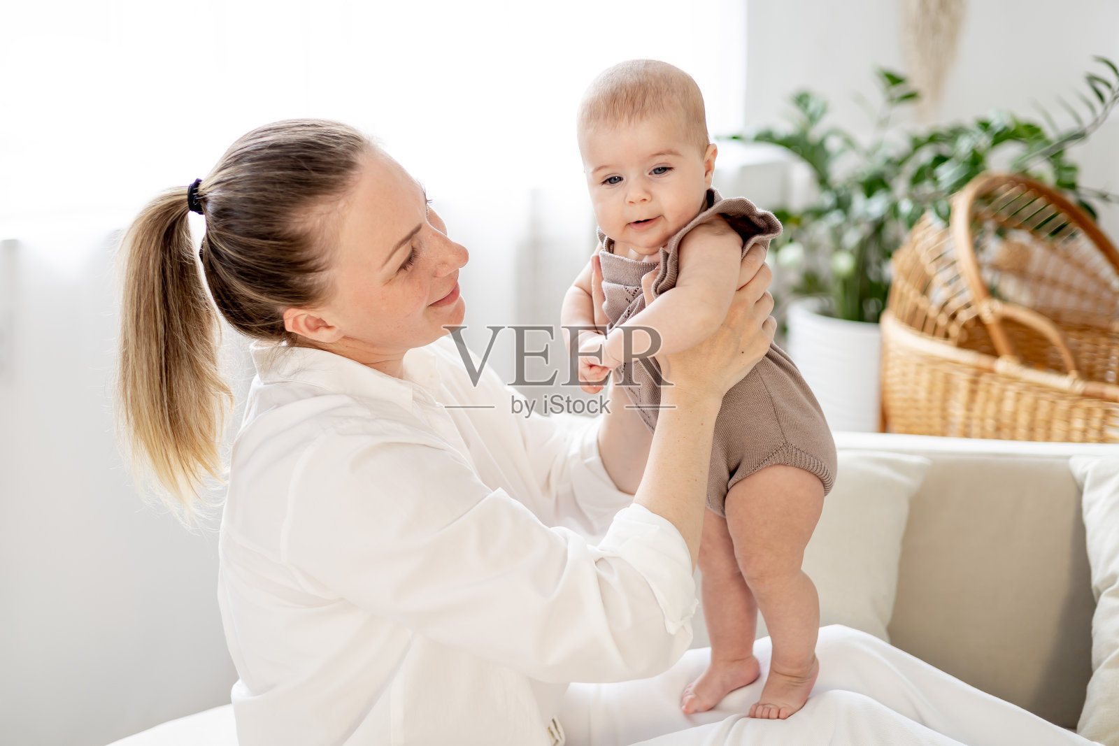 在明亮的卧室里,一位年轻的母亲抱着她刚出生的小婴儿,亲吻他,欣赏他,母亲对孩子、母亲和婴儿的爱和关怀照片摄影图片