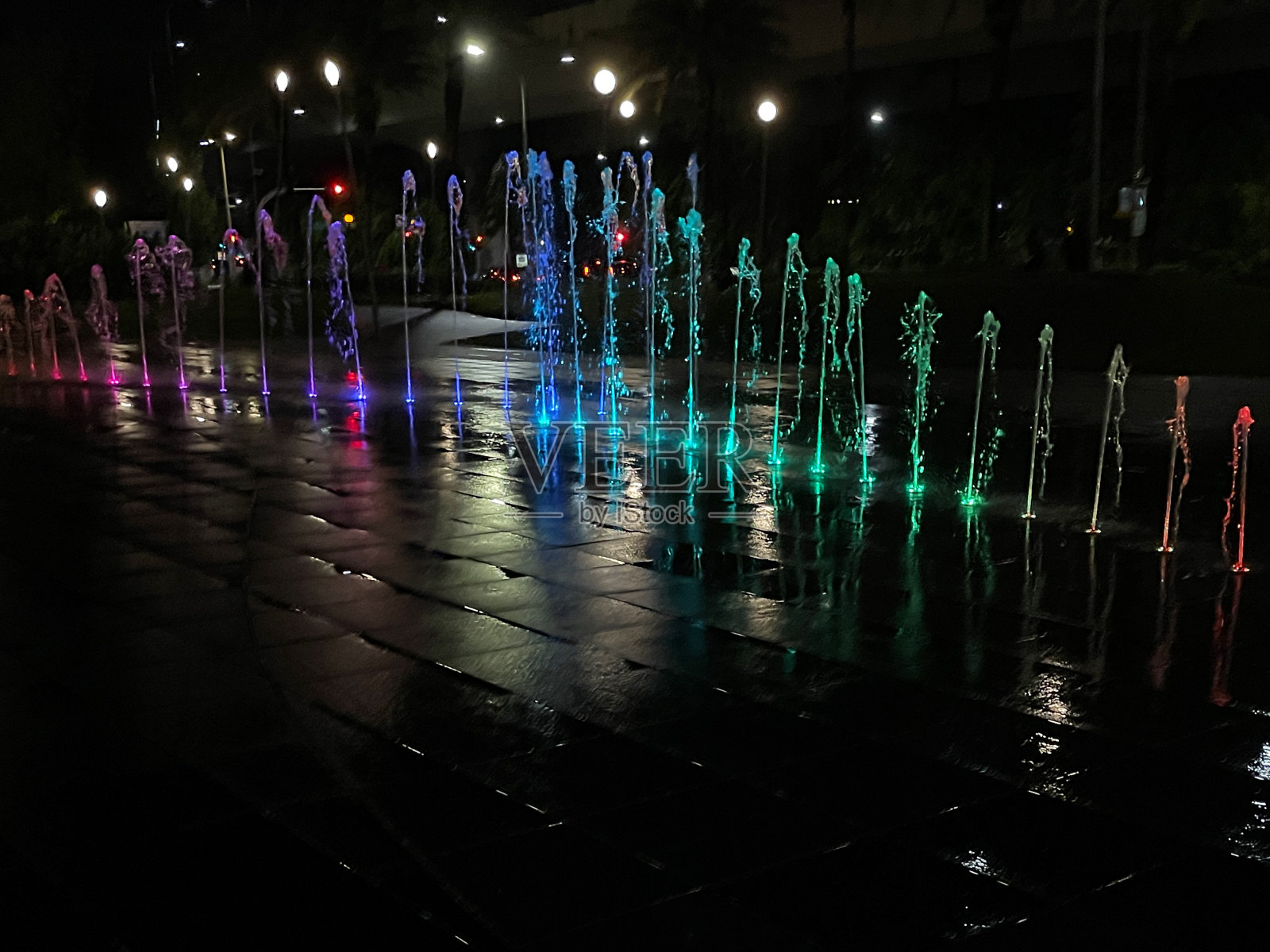 路面喷泉图像,夜间铺装板上的水柱,多色点亮的铺装水柱溅在铺装石头上,层叠的多个喷泉,水滴,聚焦于前景照片摄影图片