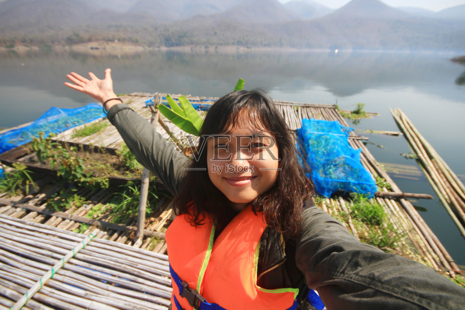 微笑的亚洲年轻女子穿着旅行的救生衣,用相机自拍,回忆假期的旅行生活。泰国女孩与泰国乡村的山和河快乐照片摄影图片