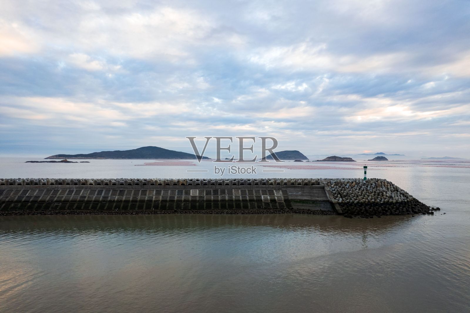 日落时分,海滨小镇附近石质长码头上的灯塔照片摄影图片