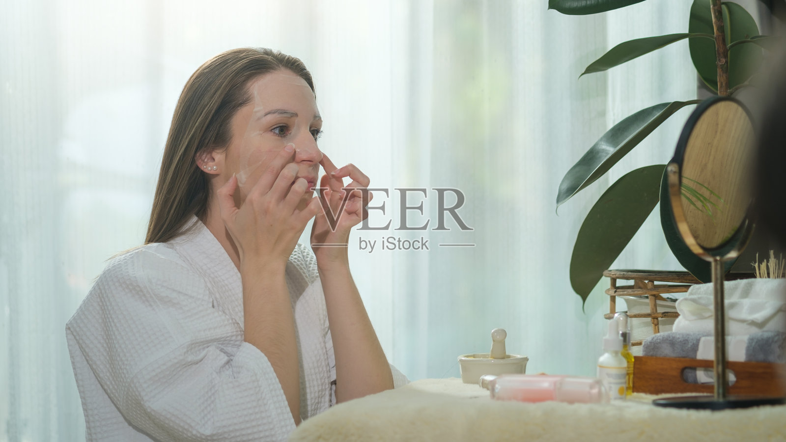 穿着浴袍的白人妇女在脸上敷面膜。美容套路,自我护理理念。照片摄影图片