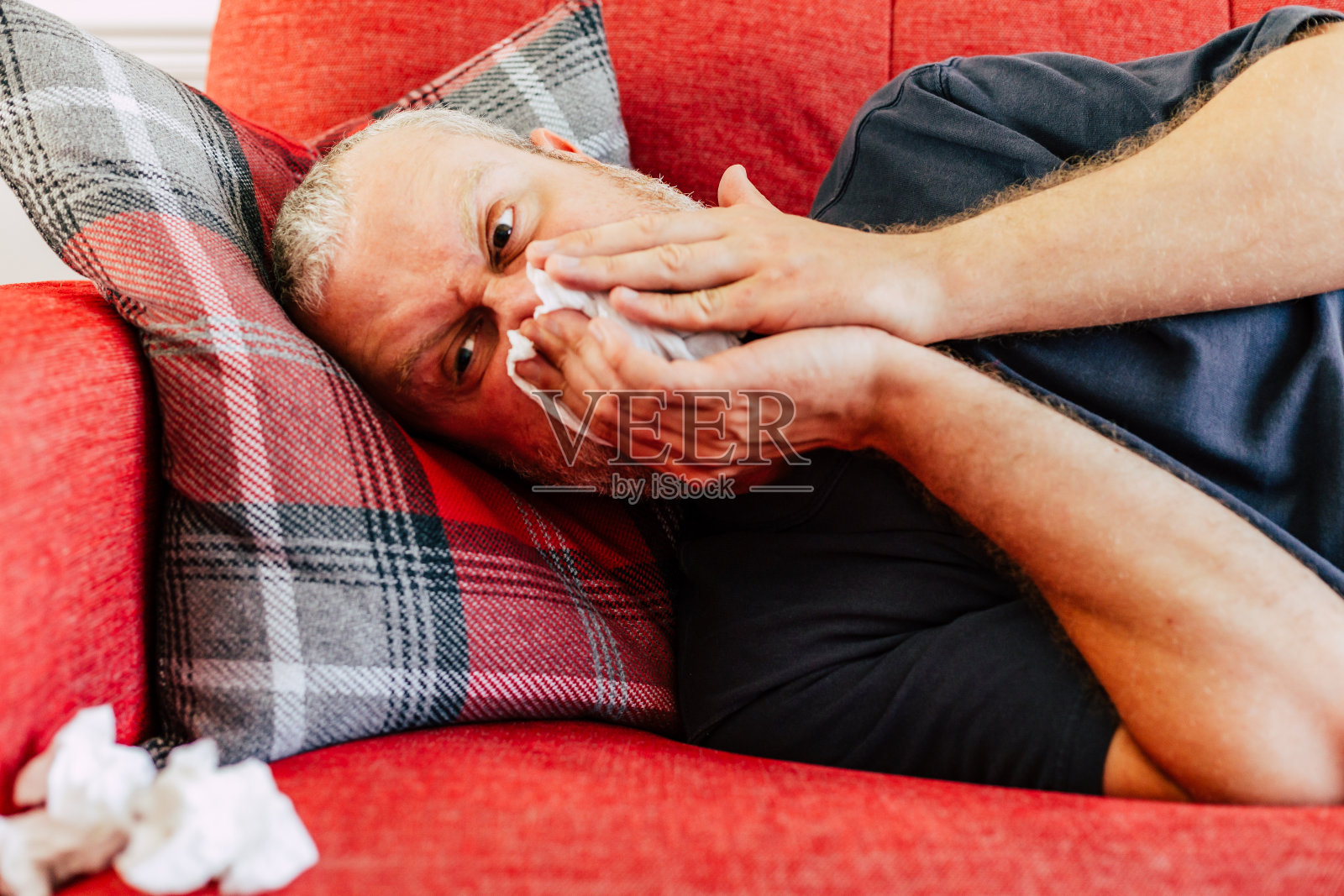 患有花粉过敏的男子躺在沙发上擤鼻涕照片摄影图片