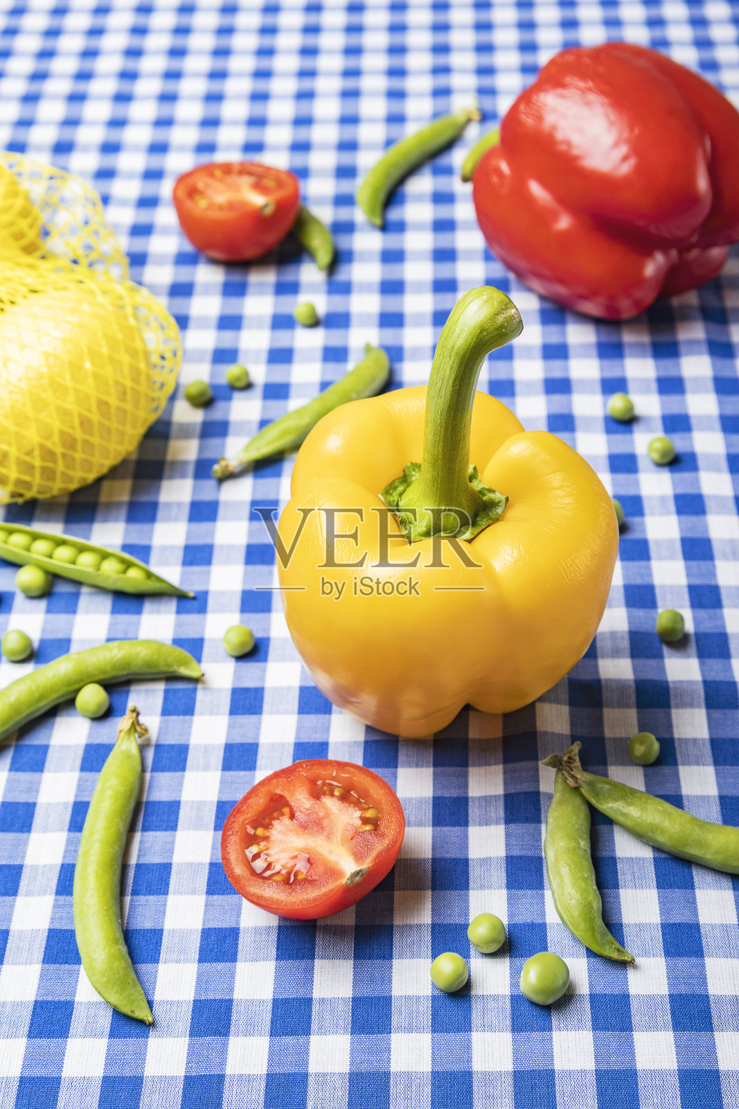 蓝色桌布上黄色、红色的甜椒、豌豆、西红柿和柠檬的垂直图像照片摄影图片