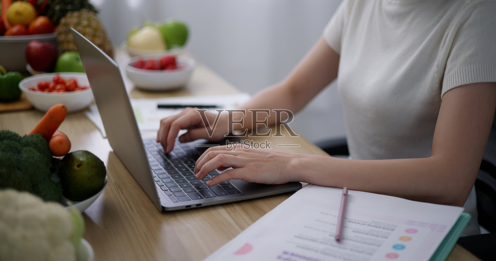 年轻的女性营养学家在笔记本电脑上用健康的水果和蔬菜工作照片摄影图片