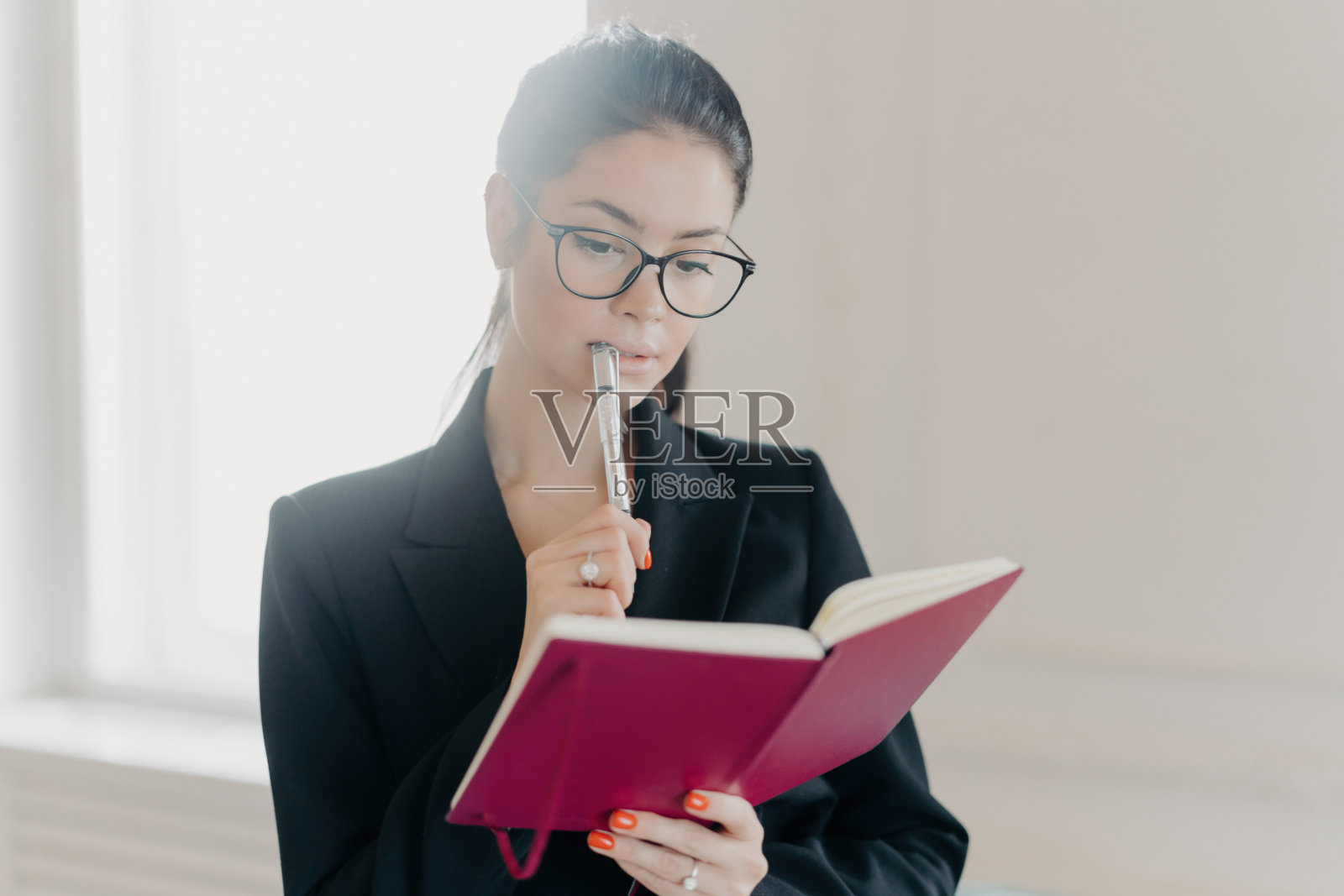 严肃熟练的高加索女性银行金融分析师检查商业信息,构思如何投资,在记事本上记笔记,戴眼镜,穿正装,在室内摆姿势照片摄影图片