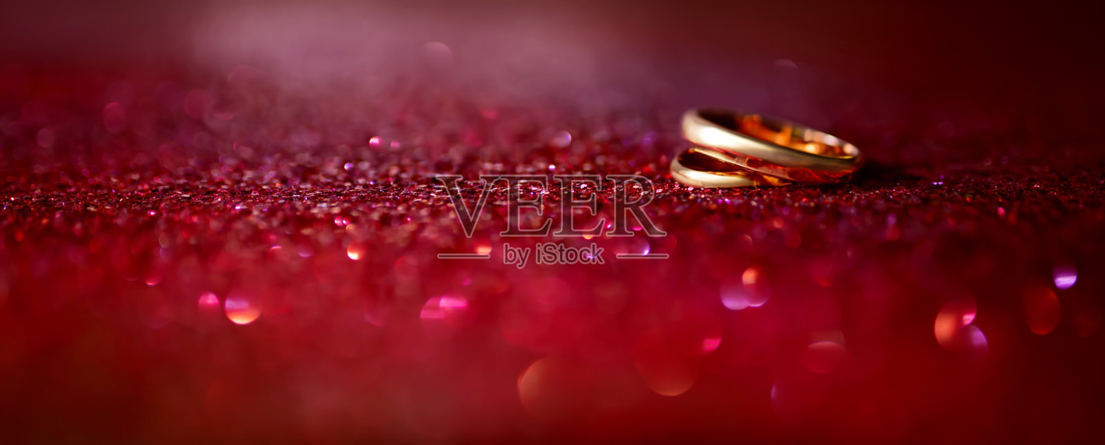 闪闪发光的红色背景上的结婚戒指照片摄影图片