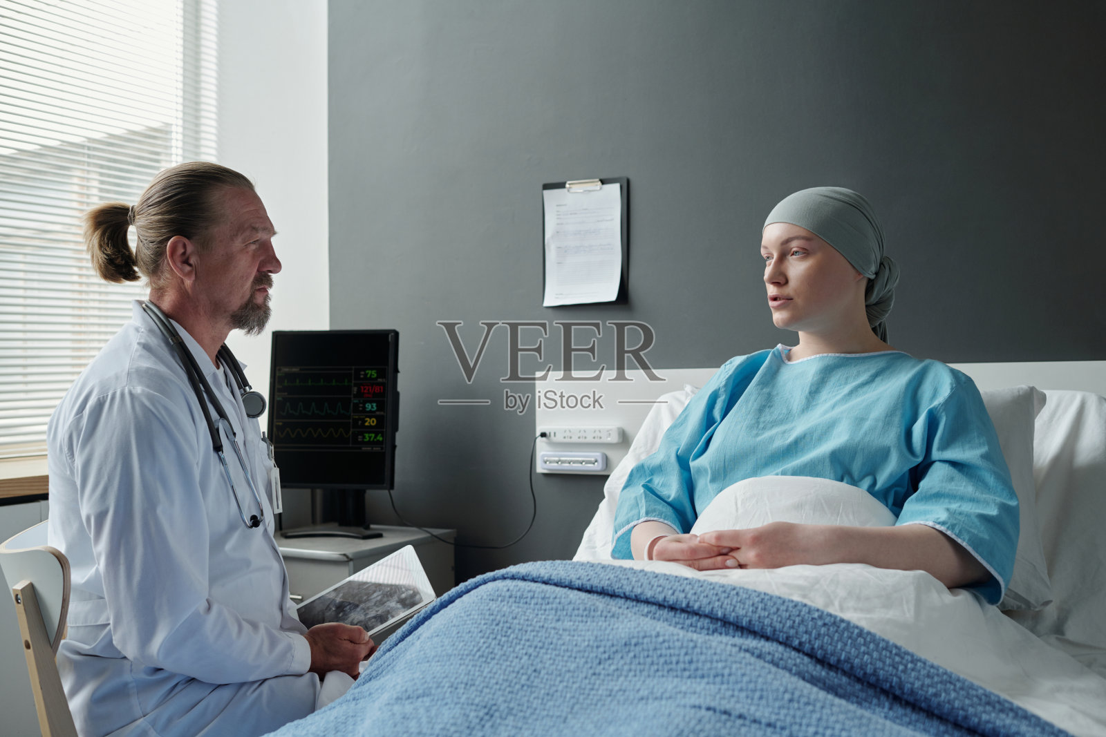 年轻的康复妇女躺在床上和经验丰富的肿瘤医生交谈照片摄影图片