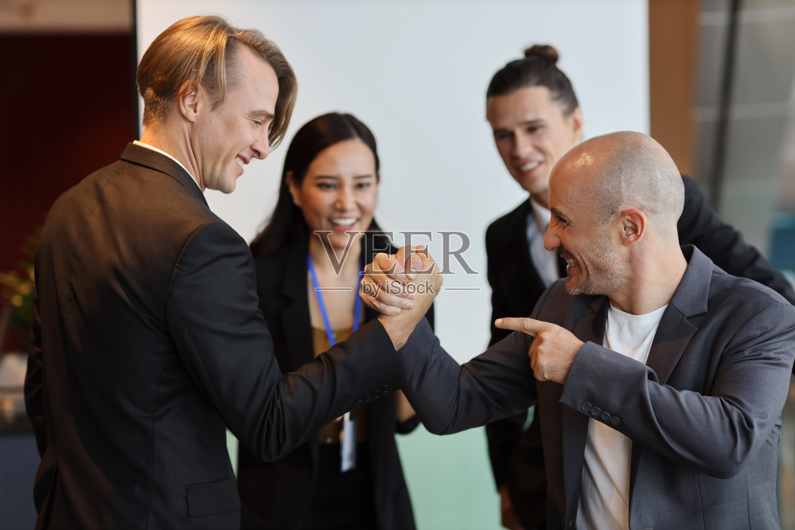 年轻的多民族专业商人在合作过程中掰手腕,签下新的商业合同后脸上带着开心的笑容。同事和一起工作的概念照片摄影图片