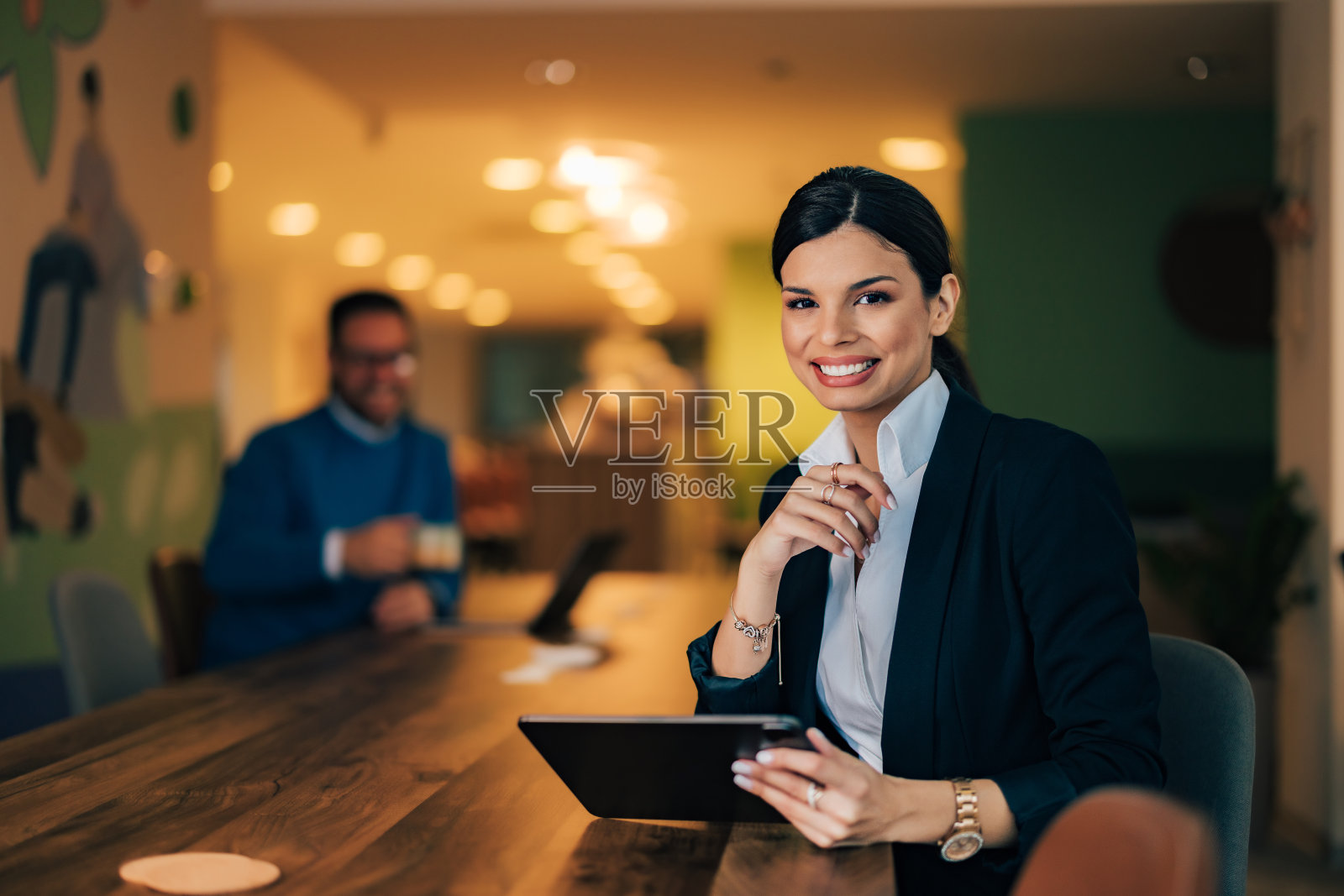 一个微笑的女人的肖像,背景是一个男同事,在办公室休息。照片摄影图片