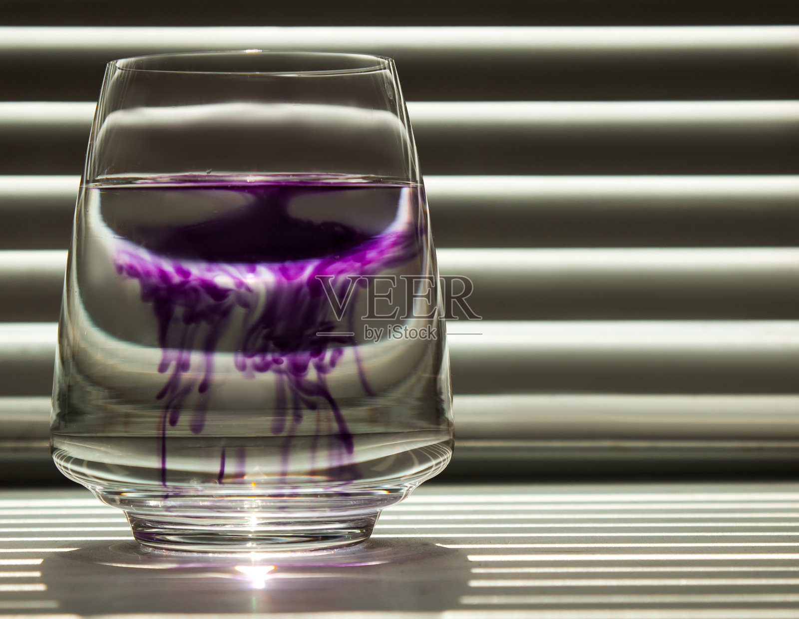 蓝色墨水在透明玻璃杯中与清水的扩散,背景是带有光线的条纹屏幕。模板,布局,背景,纹理。宏照片摄影图片