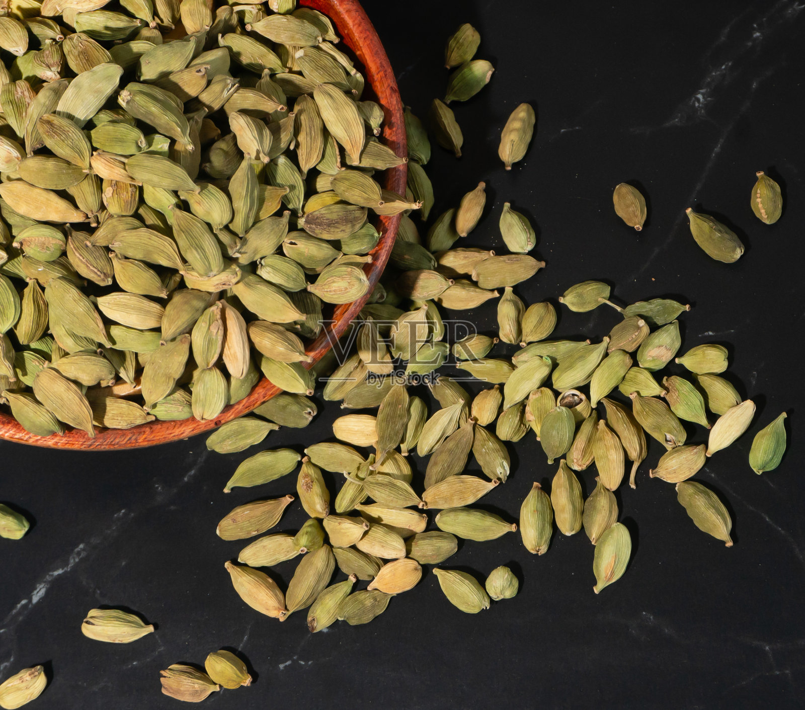 传统的香料,绿色的小豆蔻放在木碗里,散落在黑色的大理石地板上照片摄影图片