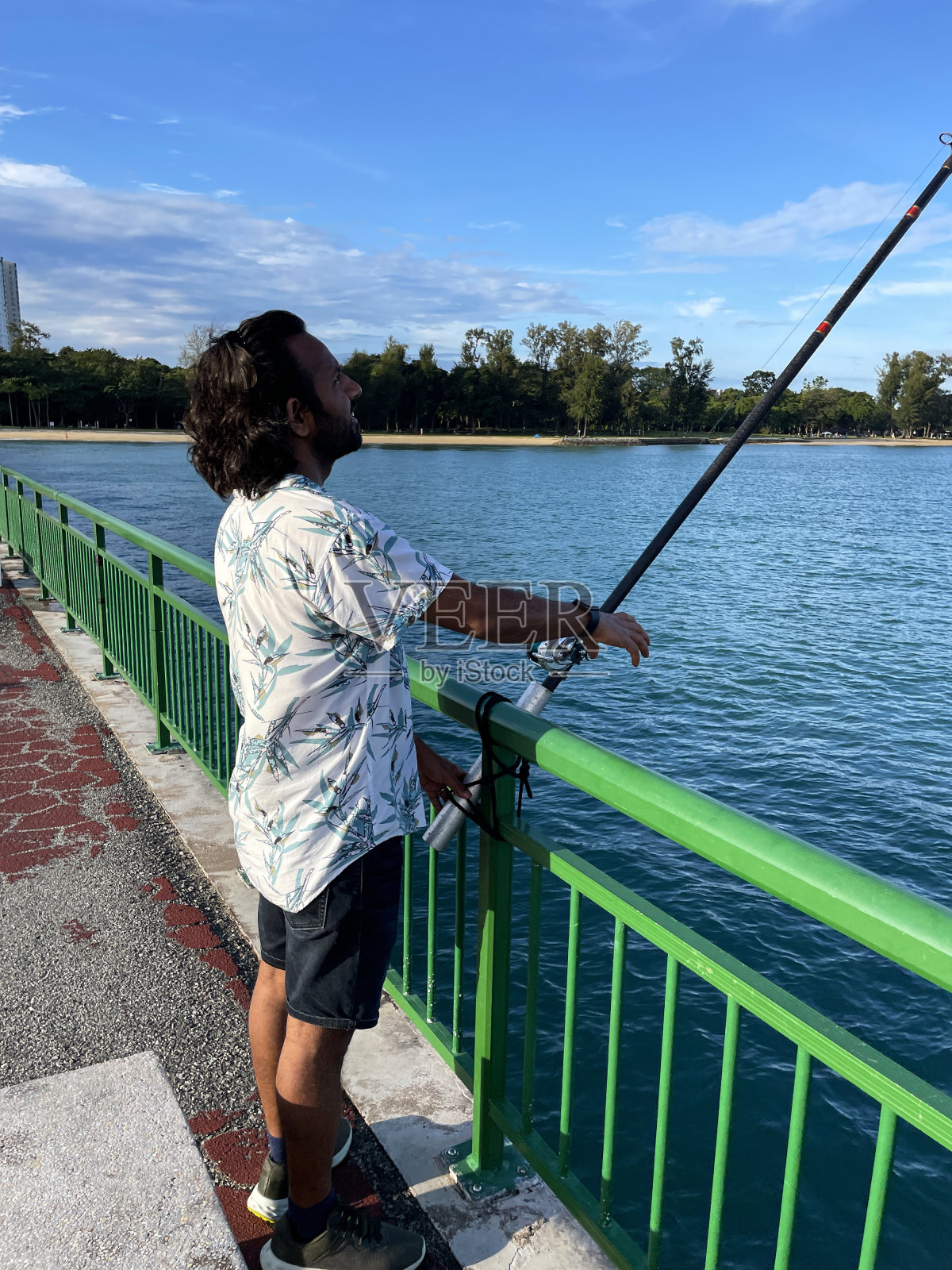 新加坡东海岸公园别德码头,印度渔民用鱼竿绑在绿色栏杆上的特写照片,波浪起伏的水面,多云晴朗的蓝天,侧面视图,聚焦于前景照片摄影图片