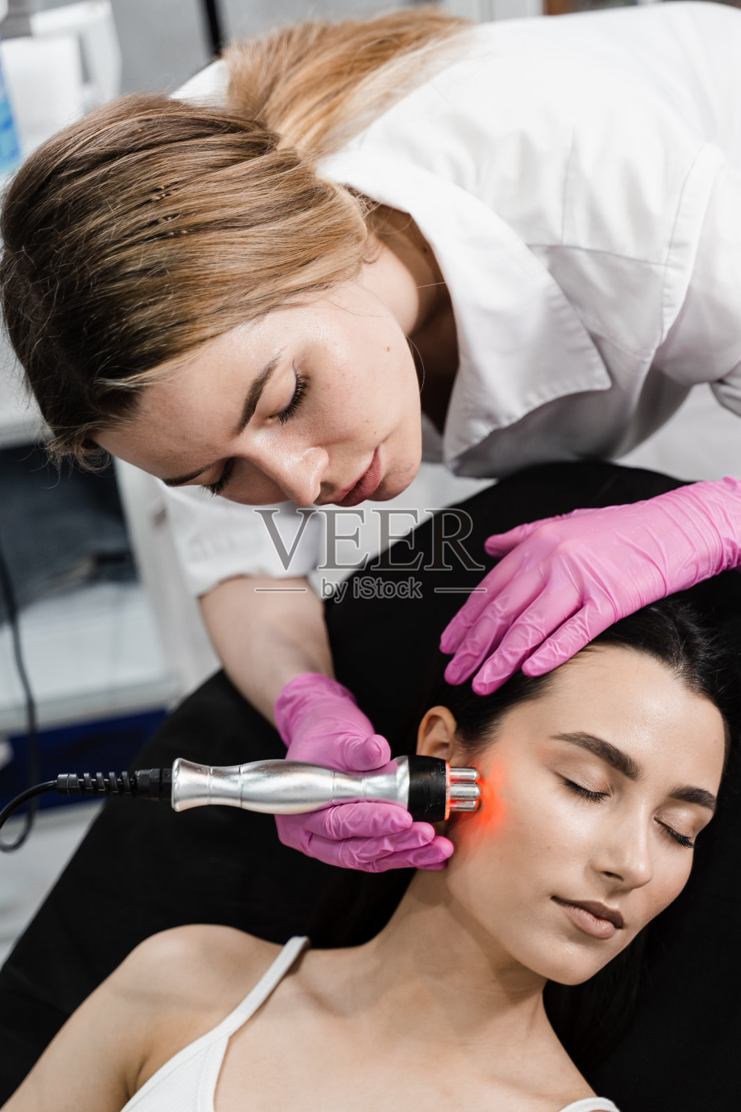 年轻女性脸上的红外线或射频红光用于硬件射频提升。在美容过程中,女孩面部皮肤的紧致和年轻化。照片摄影图片