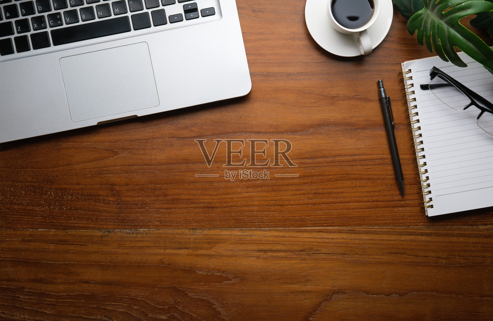 木制办公桌上的笔记本电脑、咖啡杯、记事本和眼镜的俯视图。为你的文本复制空间。照片摄影图片