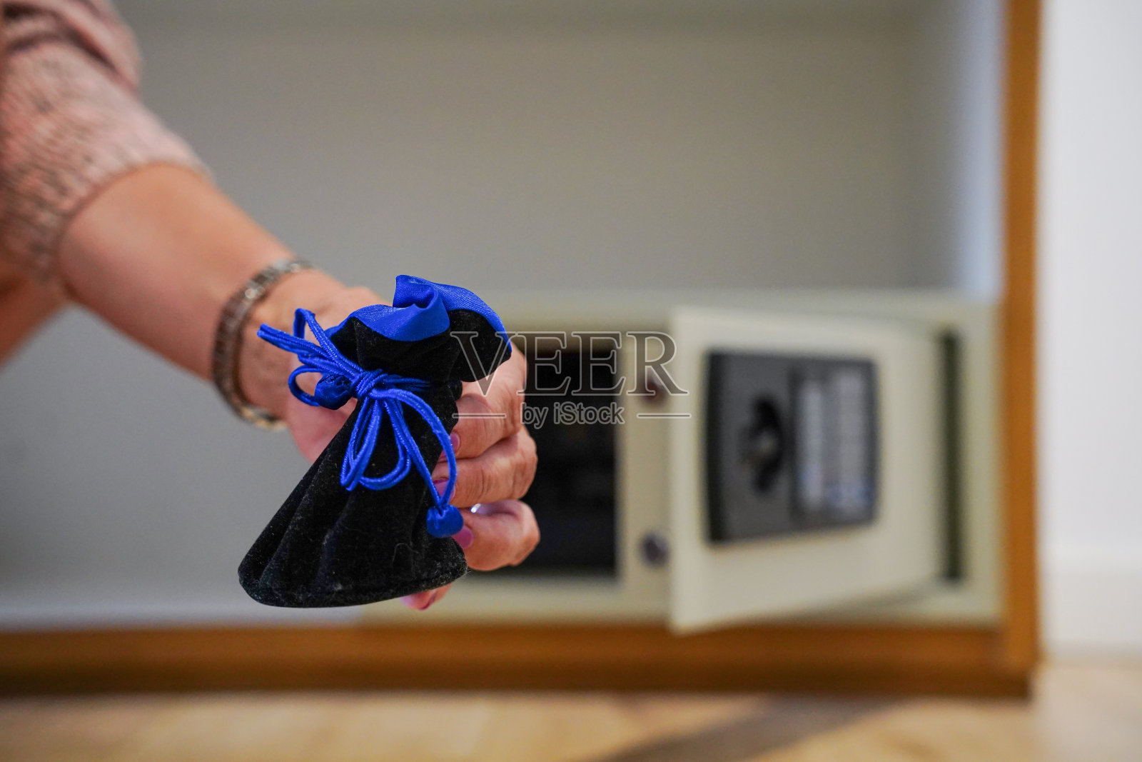 一只手把珠宝放进酒店打开的保险箱里。有代码和密码的保险照片摄影图片