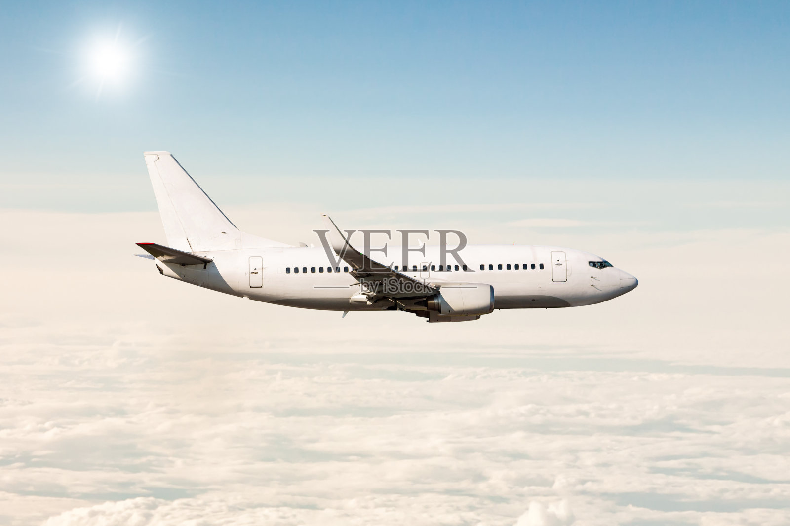 白色的喷气式客机在云层上方的空中飞行照片摄影图片