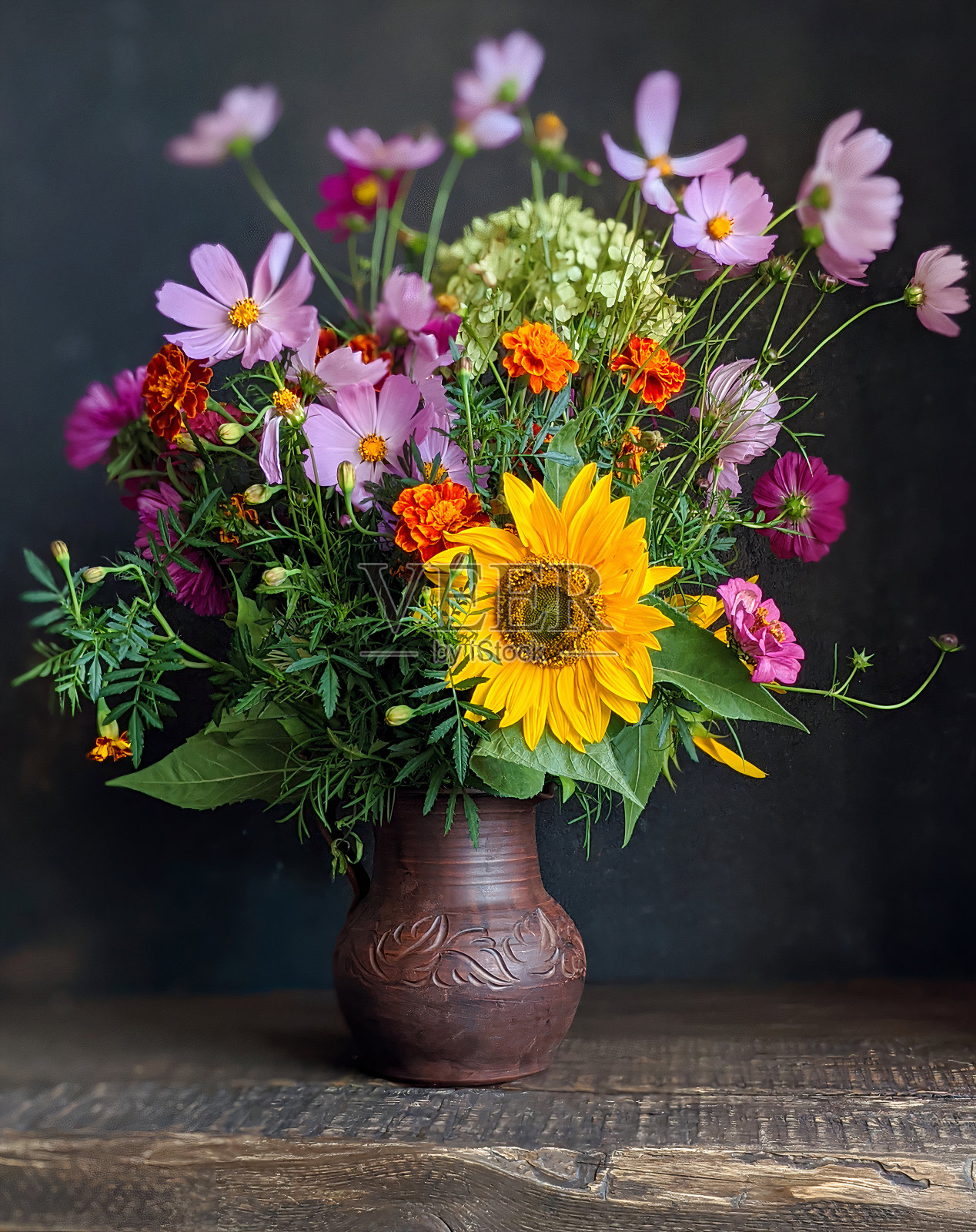 黑色背景的木桌上,一个旧罐子里放着一束花。照片摄影图片
