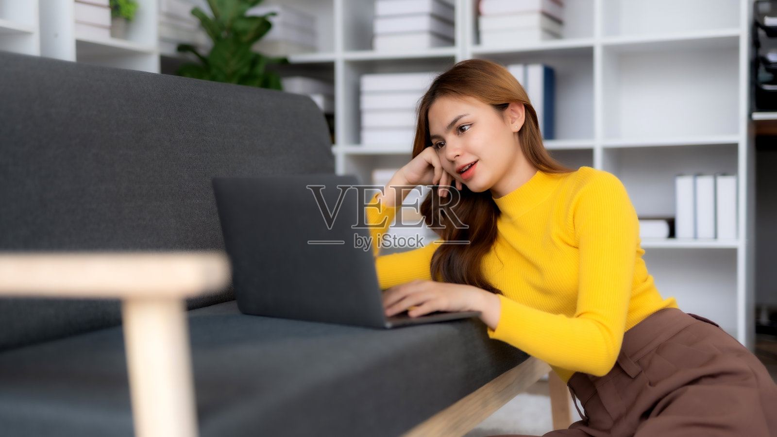 可爱的年轻女子坐在沙发上,在家里使用智能手机。女性使用手机,看电影,听音乐,网上购物,看直播。照片摄影图片