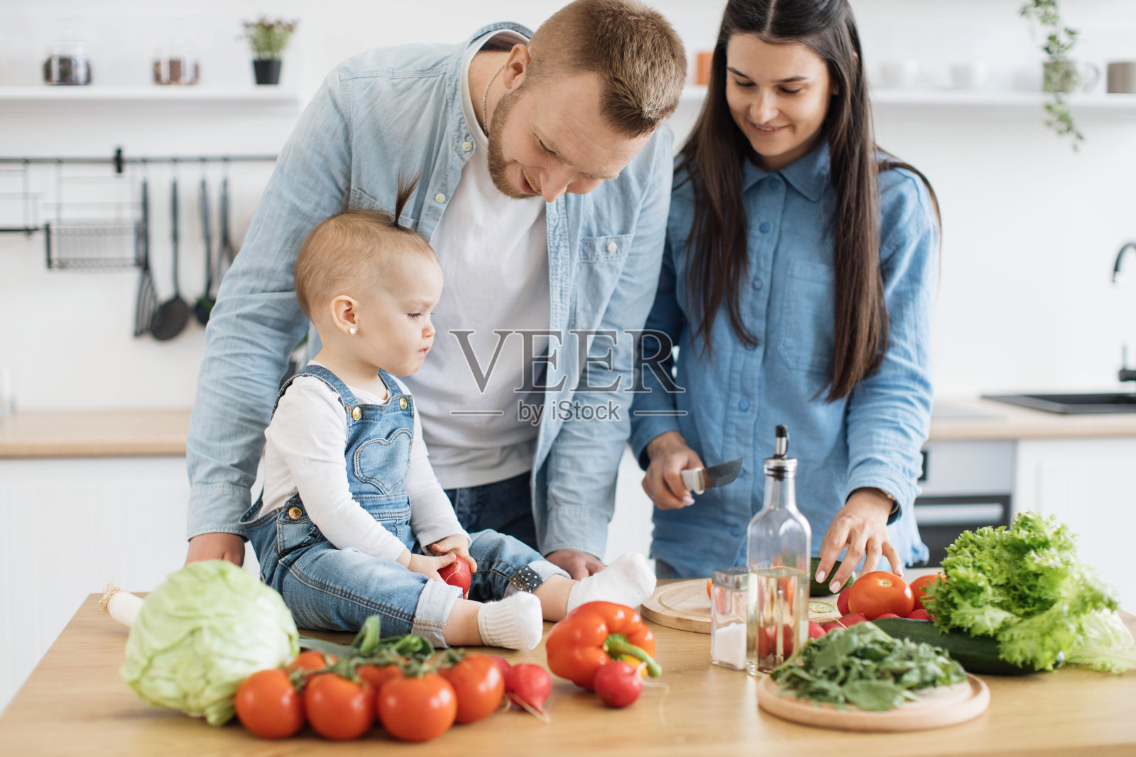 孩子嚼着新产品,妈妈在家里切蔬菜照片摄影图片