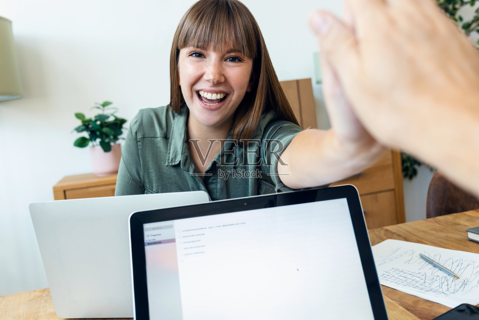 微笑的年轻女商人在办公室用笔记本电脑工作时与同事击掌。照片摄影图片