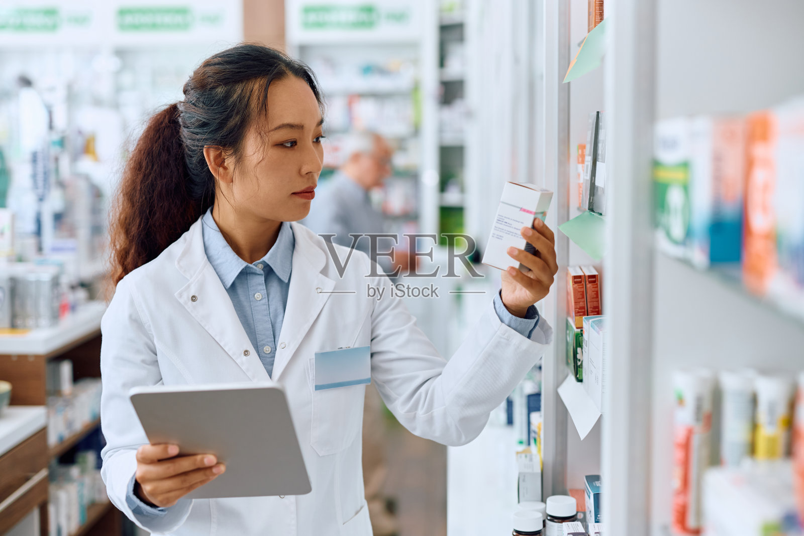 中国女药剂师在药房工作时使用数码片剂。照片摄影图片