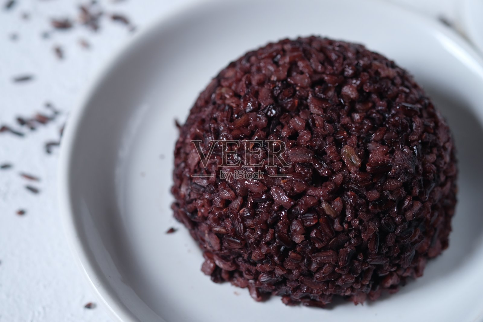 白色陶瓷盘子上的黑米。也被称为紫米。籼稻。主食。碳水化合物。照片摄影图片