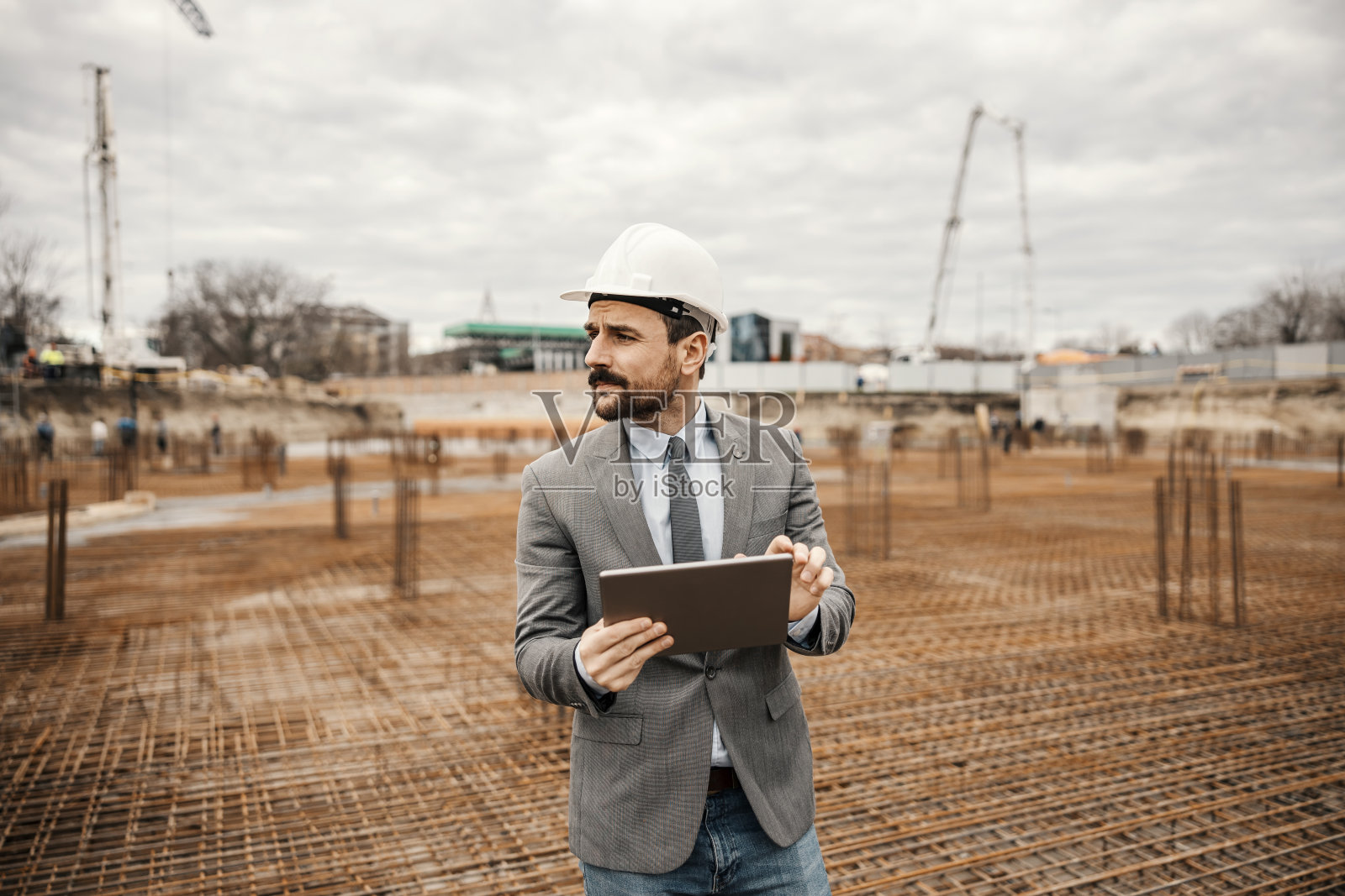 一位严肃的工程师站在建筑地基上的重建区域,在平板电脑上查看工程。照片摄影图片