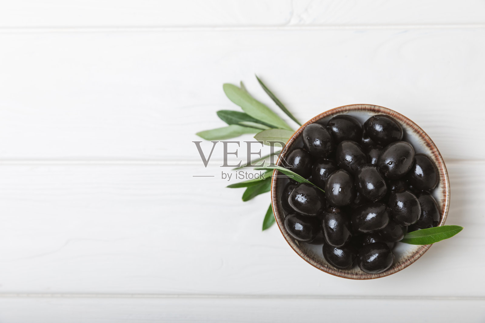 白色木制背景上的黑橄榄。碗里装着各式各样的橄榄,还有配着新鲜橄榄叶的橄榄油。副本的空间。放文字的地方。地中海食物。素食主义者。照片摄影图片