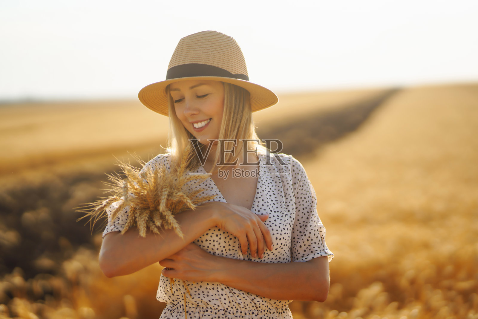时髦的年轻女子,身穿夏日连衣裙,头戴帽子,在金色的麦田里摆姿势。照片摄影图片
