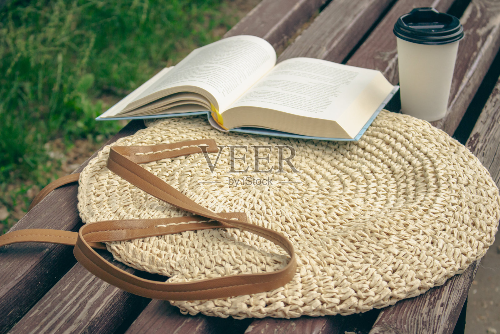 用咖啡杯在草编袋上打开书。在公园的休闲时间。打开书和咖啡坐在长凳上。夏天放松。舒适的生活方式。阅读之外。在长凳上模拟杯子。照片摄影图片