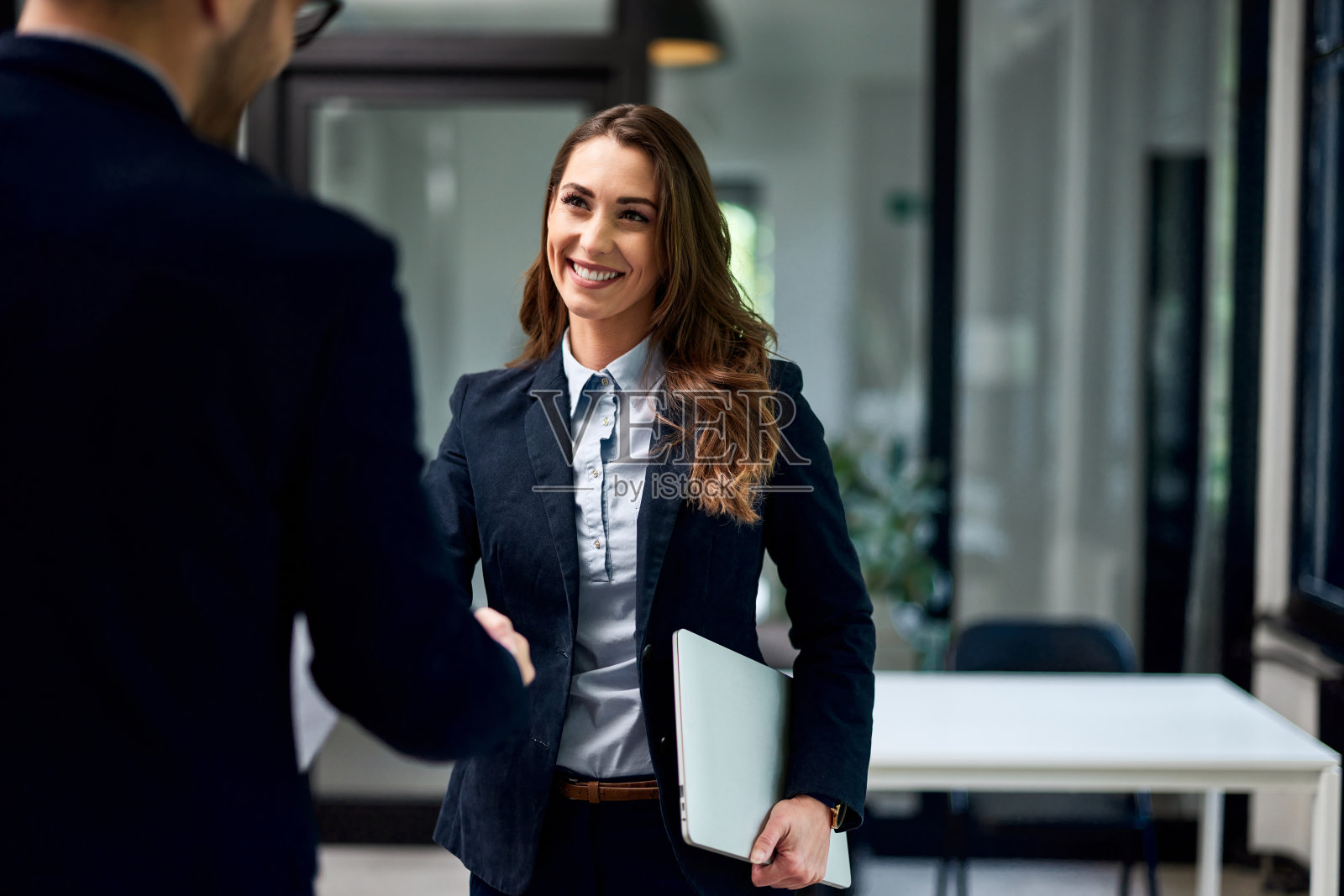 一位面带微笑的女商人拿着一份文件和一位男同事握手。照片摄影图片